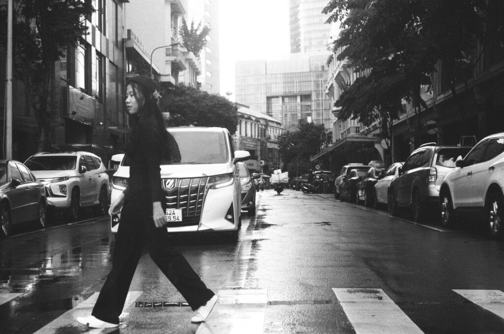 Asian woman crossing street in urban monochrome setting with cars.
